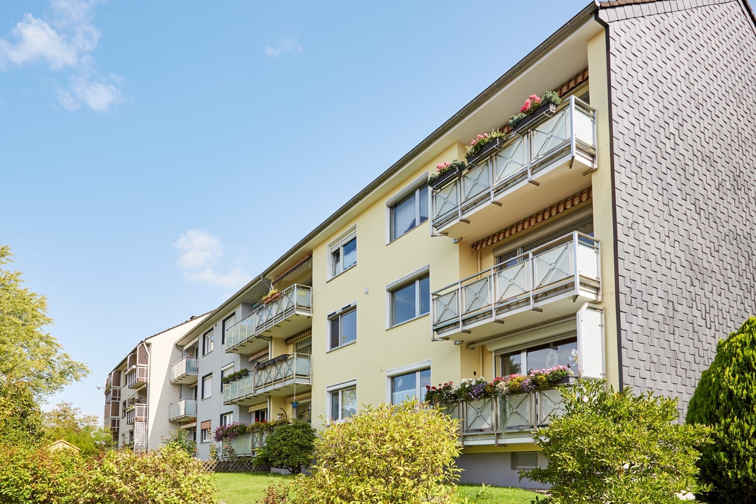Wohnhaus mit Balkonen, Rasenfläche und Baumbestand
